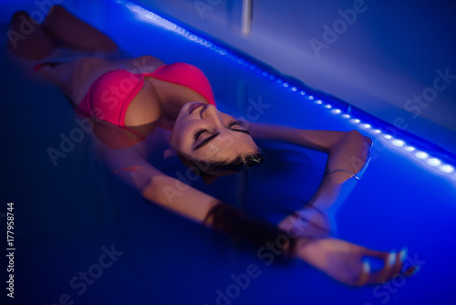 Beautiful tanned woman in pink swimwear relaxing in swimming pool spa photo