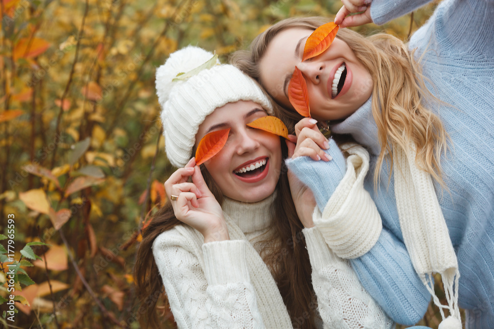 Naklejka premium Beautiful girlfriends on the autumn background having fun. Cheerful women in the fall time. Smiling girlfriends outdoors