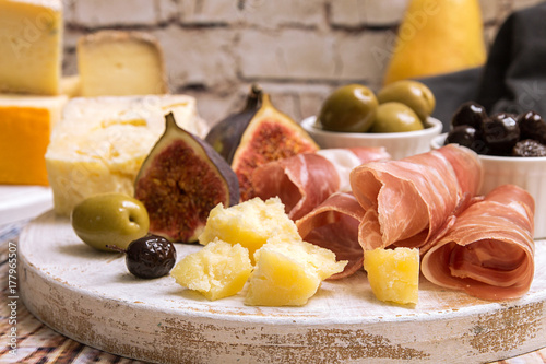 Slices of prosciutto, pieces of cheese, olives, pear, honey and figs on white wooden cutting board photo