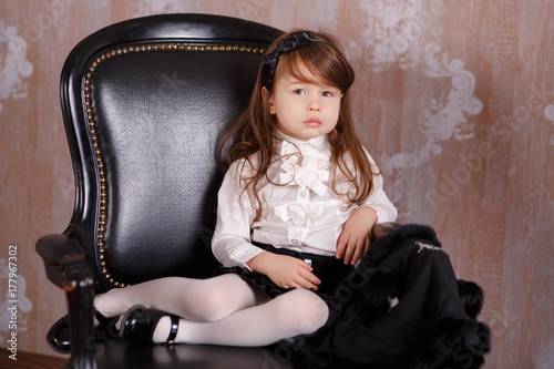 Young brunette dolly lady girl stylish dressed like a boss in white official shirt black skirt posing sitting in studio on black leather chair with pout lips and pink cheeks. photo