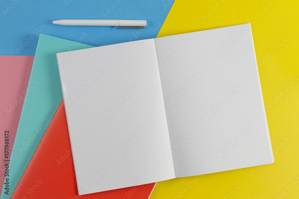 Open notebook, white pen and colorful notebooks on blue and yellow background Open notebook, white pen and colorful notebooks on blue and yellow background