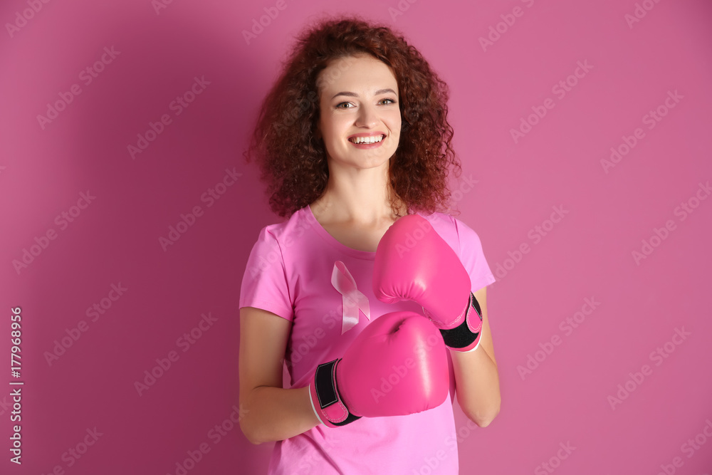 Young woman in pink t-shirt and boxing gloves on color background. Breast cancer awareness concept Young woman in pink t-shirt and boxing gloves on color background. Breast cancer awareness concept