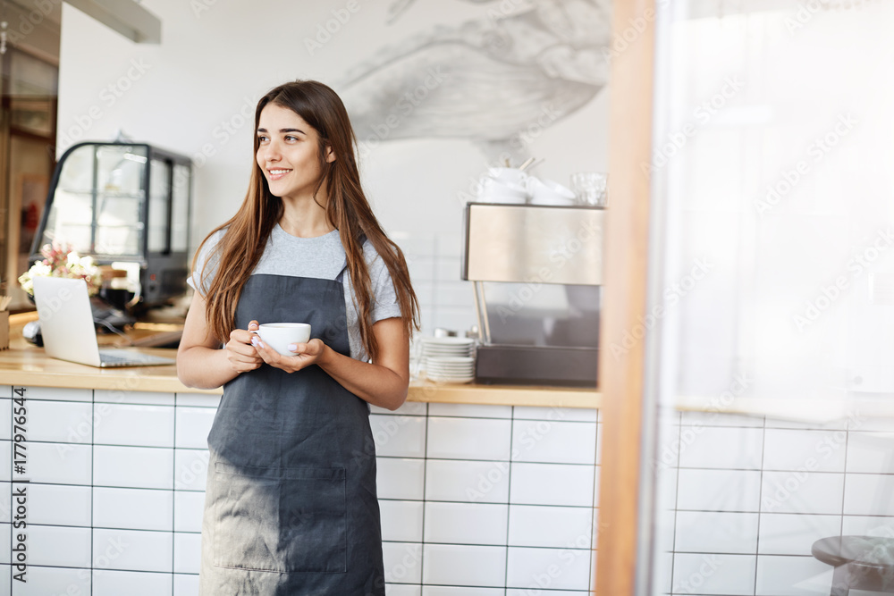 Portrait of young female barista enjoying morning coffee. Responsible and beautiful employee is a key to success in cafe. Portrait of young female barista enjoying morning coffee. Responsible and beautiful employee is a key to success in cafe.