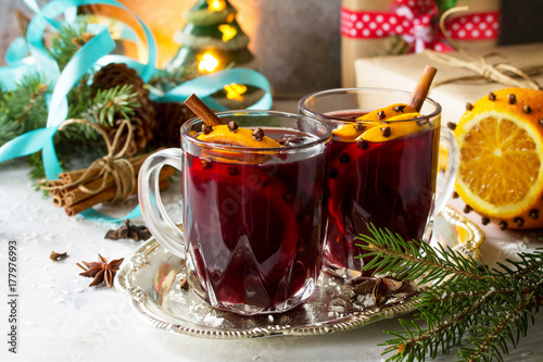 Homemade Christmas cocktail mulled wine red wine with cinnamon sticks, oranges and cloves, served in two cups on a gray stone or slate.