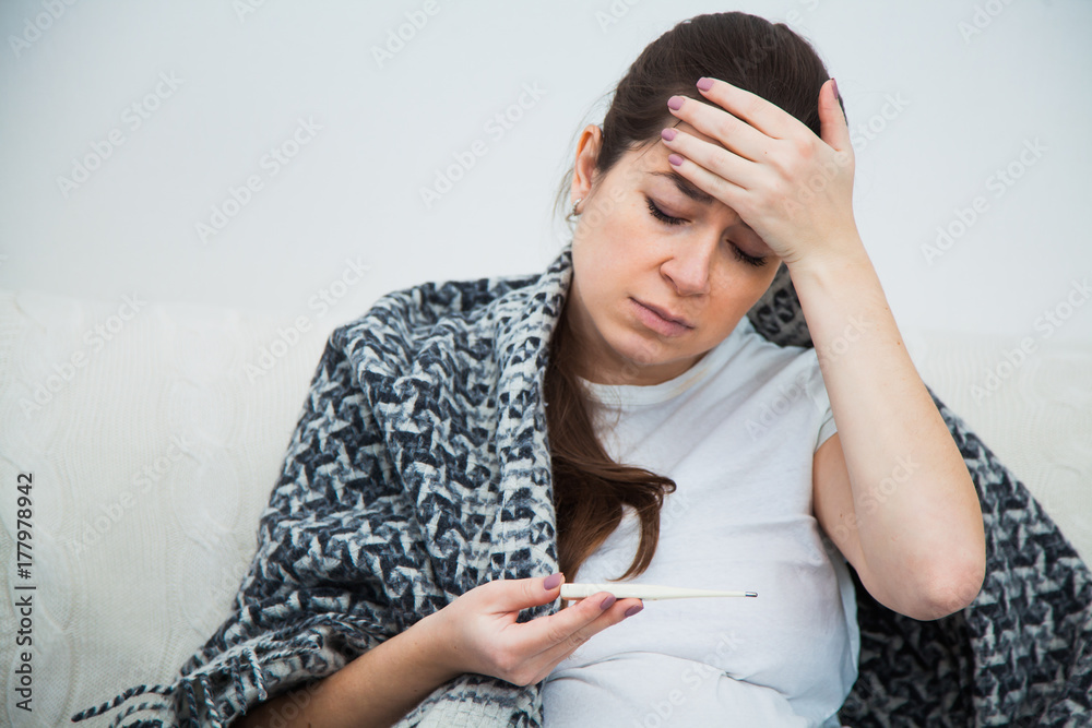 Young pregnant woman feel sick, high fever, sitting on sofa indoors Young pregnant woman feel sick, high fever, sitting on sofa indoors