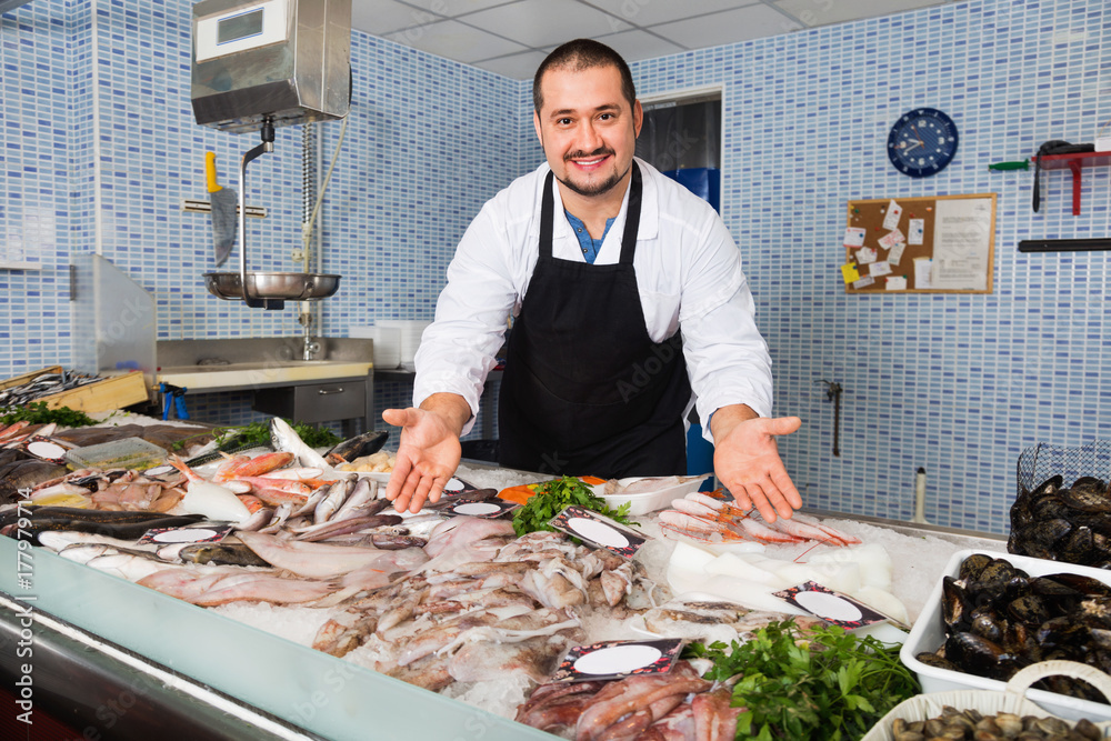 Seller in black apron showing fish on his counter
