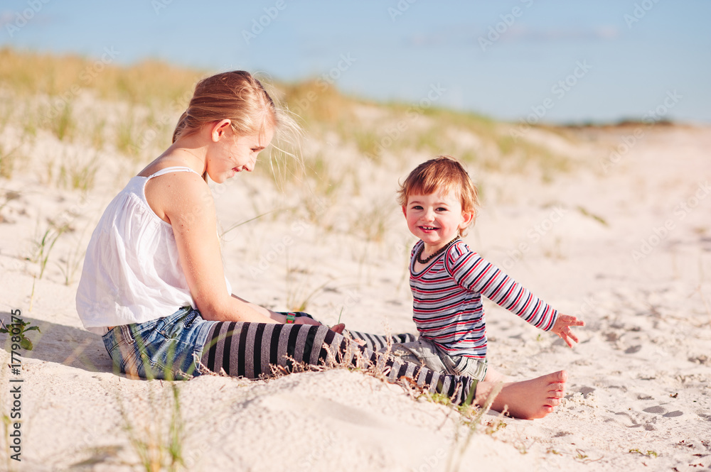 Pre-teen girl playing with a toddler in sand dunes at the beach Pre-teen girl playing with a toddler in sand dunes at the beach