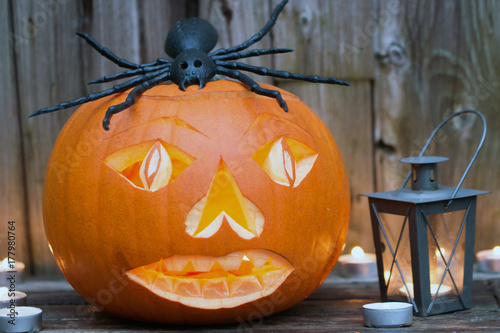 Gruseliger Halloween Kürbis mit Spinne als Dekoration für den 31.Oktober vor Holzhintergrund