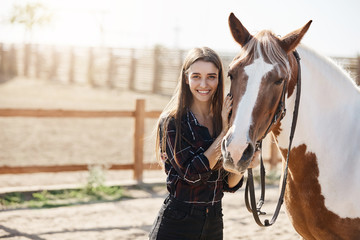 Portrait of young girl standing next to a horse looking at camera smiling.