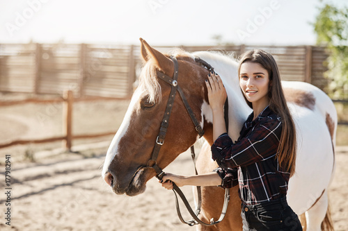 Young female veterinarian calming down an ill horse looking at camera smiling.