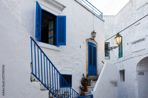 View of a narrow street with a blue door and blue window in the romantic ancient town of Ostuni