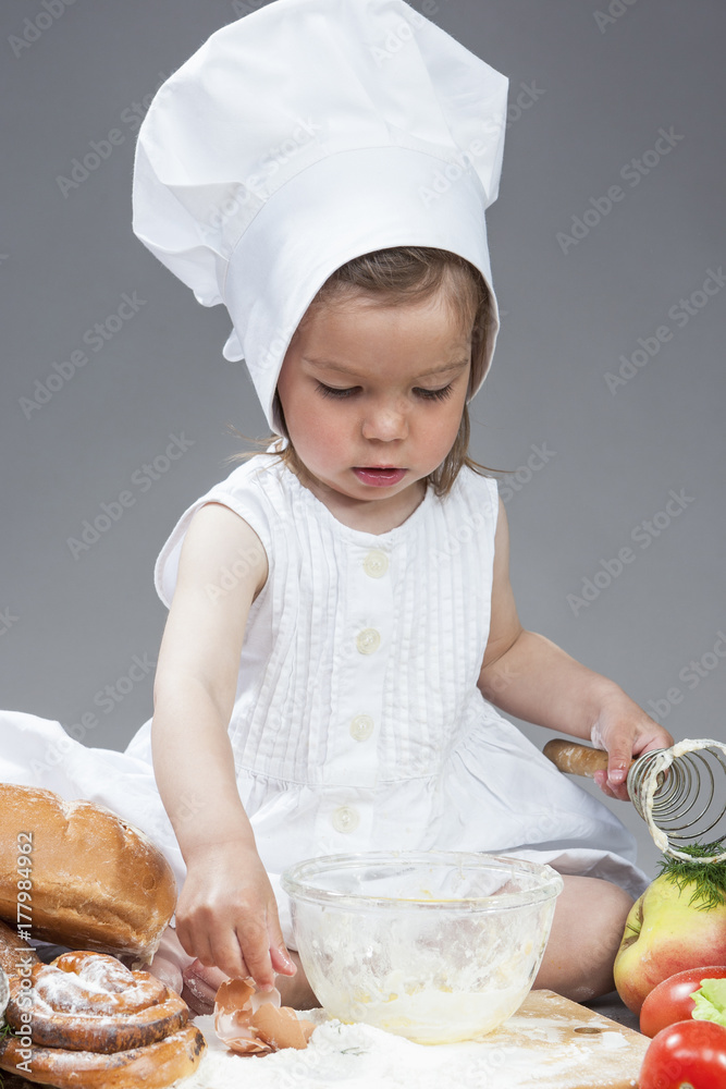 Caucasian Girl In Cook Uniform Working With Kitchen Glassware with Whisk In Studio Environment. With Vegetables and Fruits on Background. Caucasian Girl In Cook Uniform Working With Kitchen Glassware with Whisk In Studio Environment. With Vegetables and Fruits on Background.