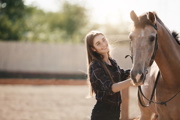 Young female farm owner taking care about a horse on an animal ranch on a summer day.