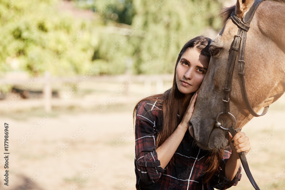 Obraz premium Portrait of young woman and a horse. Longhaired beautiful girl holding and calming down a stallion.