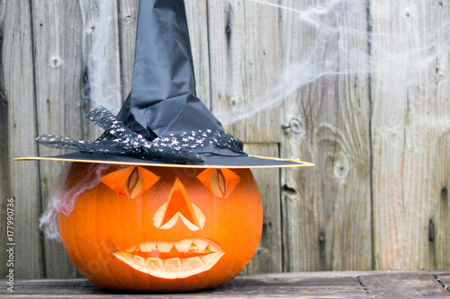 Gruseliger Halloween Kürbis mit Hut und Spinnweben vor Holzhintergrund für den 31.Oktober