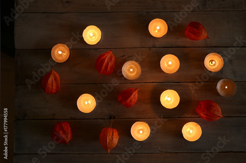 Burning candles with plant decorations in the darkness. Small round tea light candles with chinese lanterns on wooden table top view..