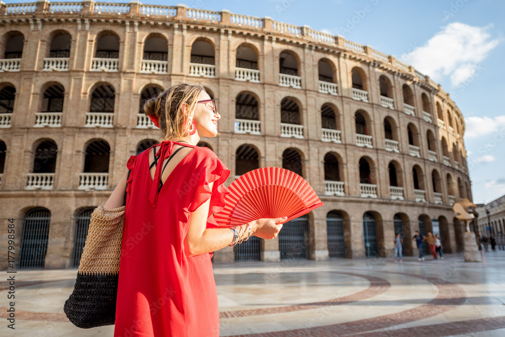 Woman in red dress with spanish hand fan stnading back in front of the bullring amphitheatre in Valencia city, Spain