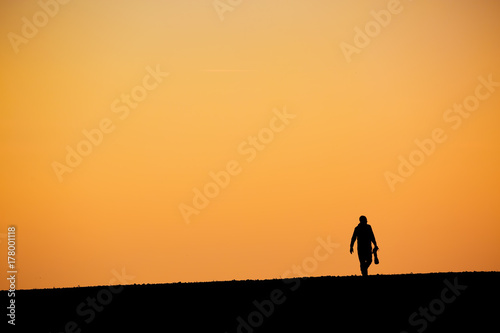 Silhouette man with big telephoto lens against orange sunset sky background.
