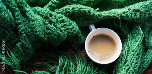 the panorama of top view of cup of hot coffee and warm green scarf. Concept of coziness and warmth