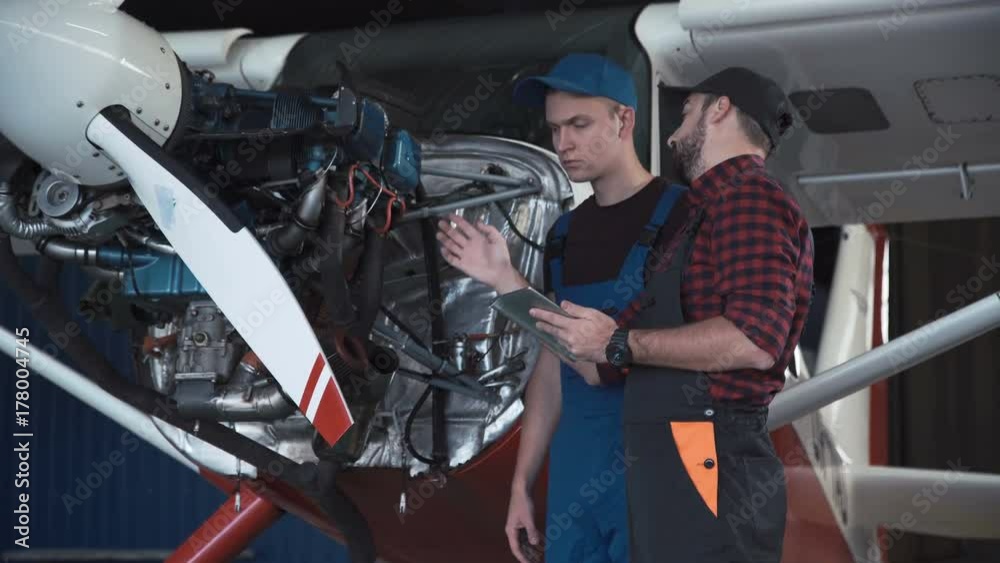 Two flight mechanics doing a pre flight check or maintenance on a small single engine aircraft in a hangar in a close up view of them working on the engine.