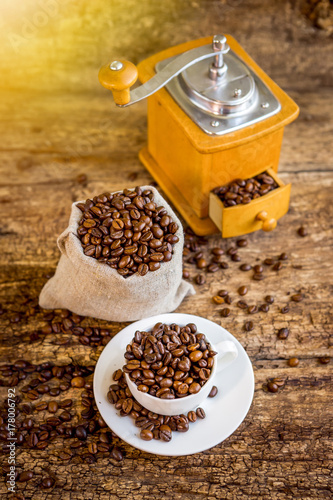 Cup of coffee beans. Coffee grinder and bag with coffee beans in the background.