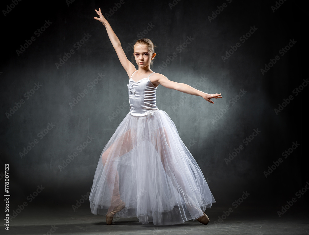 Fototapeta premium Beautiful young ballerina is dancing in the studio on a dark background. A little dancer. Ballet dancer.
