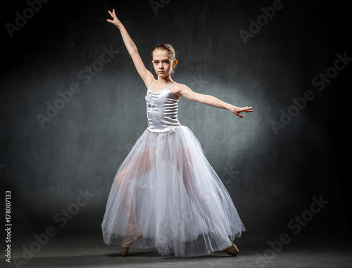 Beautiful young ballerina is dancing in the studio on a dark background. A little dancer. Ballet dancer.