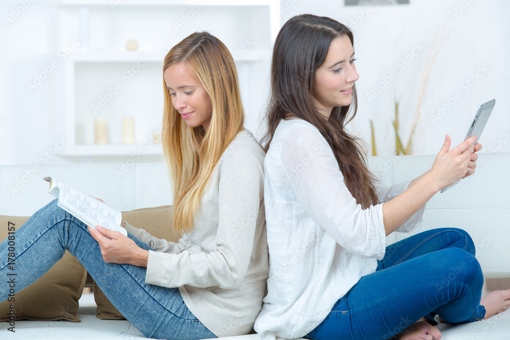 two friends sitting on sofa and reading book at home two friends sitting on sofa and reading book at home