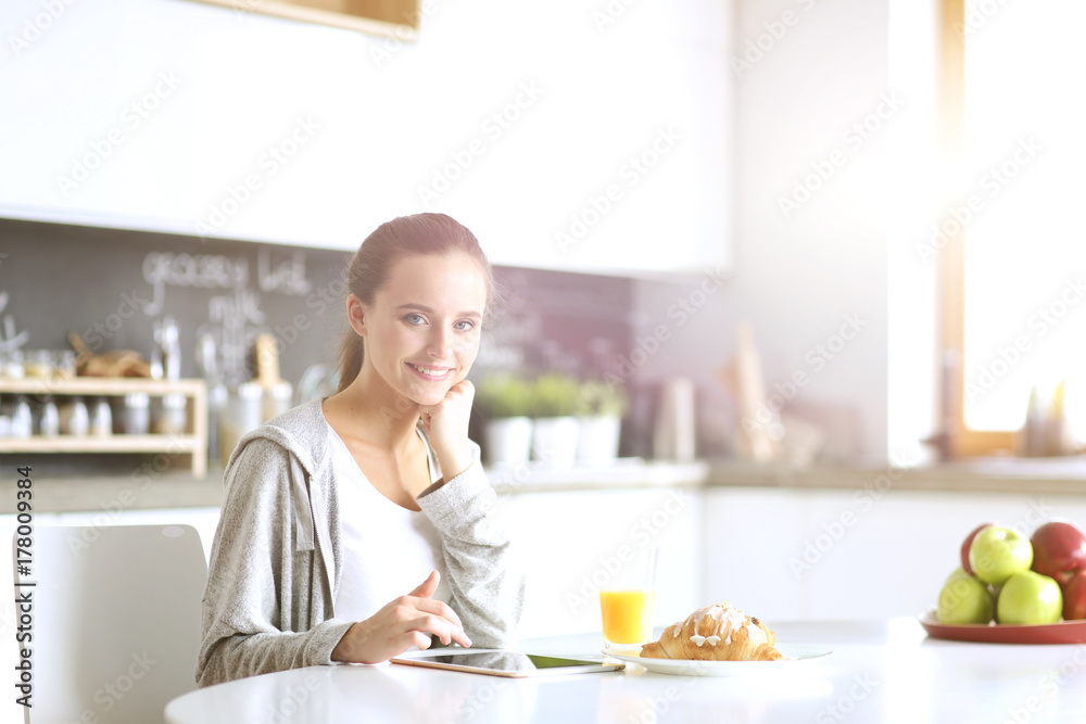 Young woman with orange juice and tablet in kitchen.
