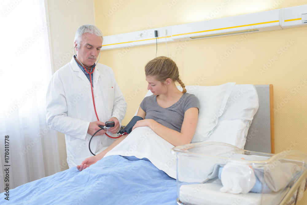 Obraz premium male doctor checking pregnant woman blood pressure in hospital