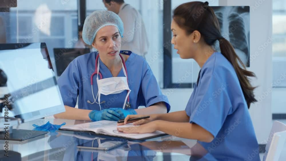 Hospital doctor prepared for surgery discussing patient notes with colleague. Hospital doctor prepared for surgery discussing patient notes with colleague.