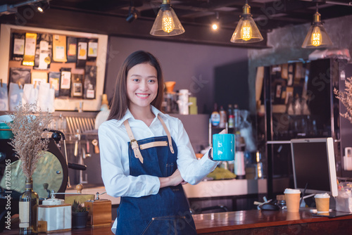 Beautiful asian barista holding coffee cup and smiles in her cafe