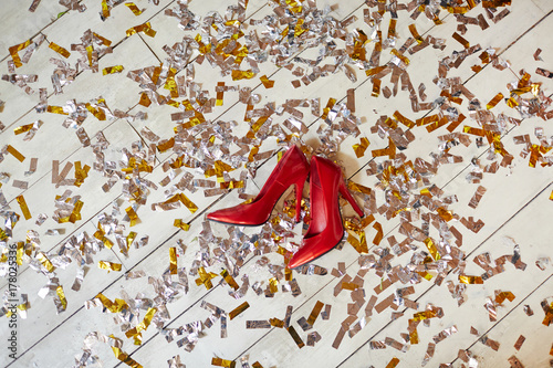 Pair of red high-heeled stylish female shoes on white wooden floor covered by confetti photo