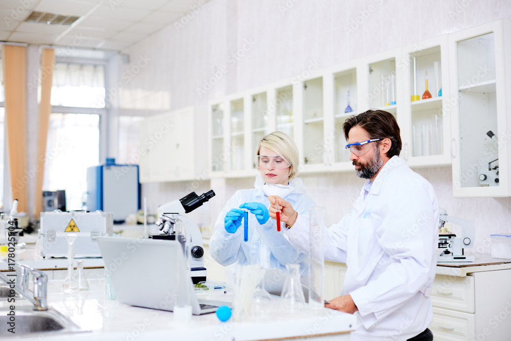 Male and female chemists analyzing new liquids or vaccine in flasks Male and female chemists analyzing new liquids or vaccine in flasks
