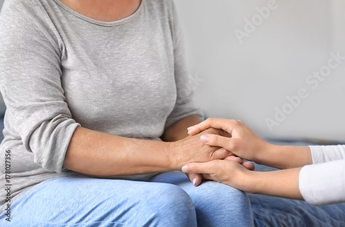 Mature and young women holding hands indoors. Elderly care concept