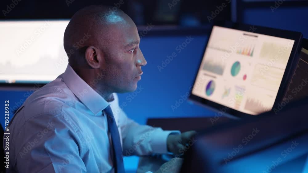  Computer expert working in a dark room surrounded by computer screens