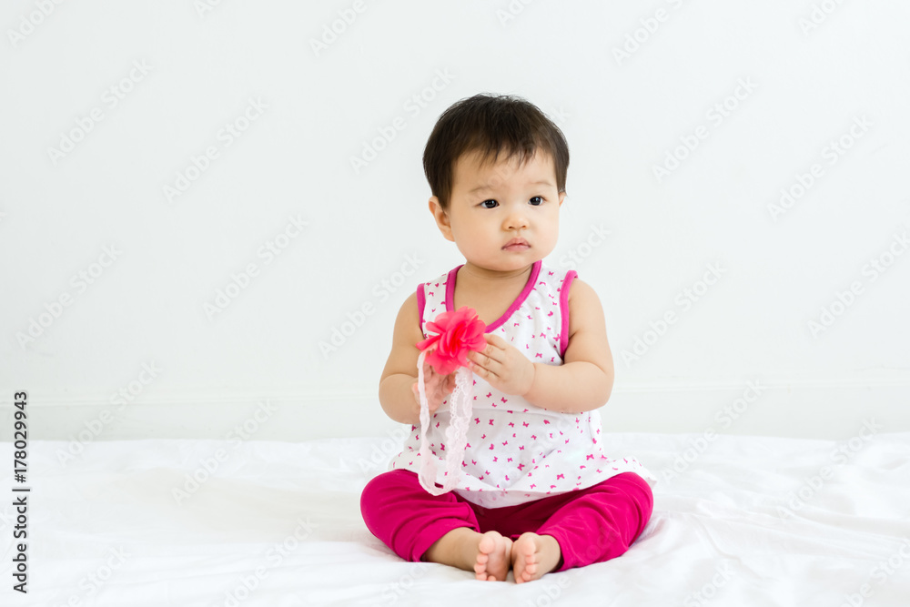 Portrait of adorable baby sitting on a white floor and holding head band Portrait of adorable baby sitting on a white floor and holding head band