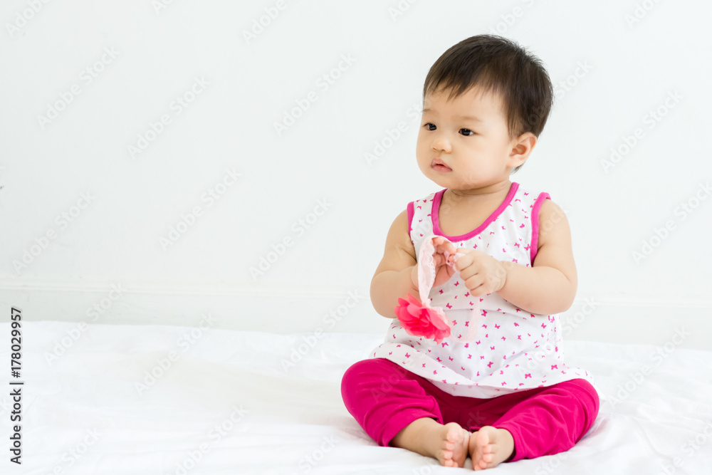 Portrait of adorable baby sitting on a white floor and holding head band Portrait of adorable baby sitting on a white floor and holding head band