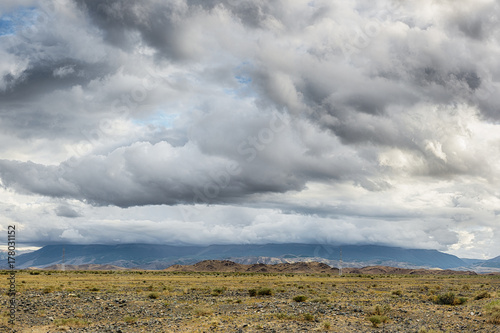 panoramic view of beautiful meadow at foot of mountains with grey storm clouds in sky 