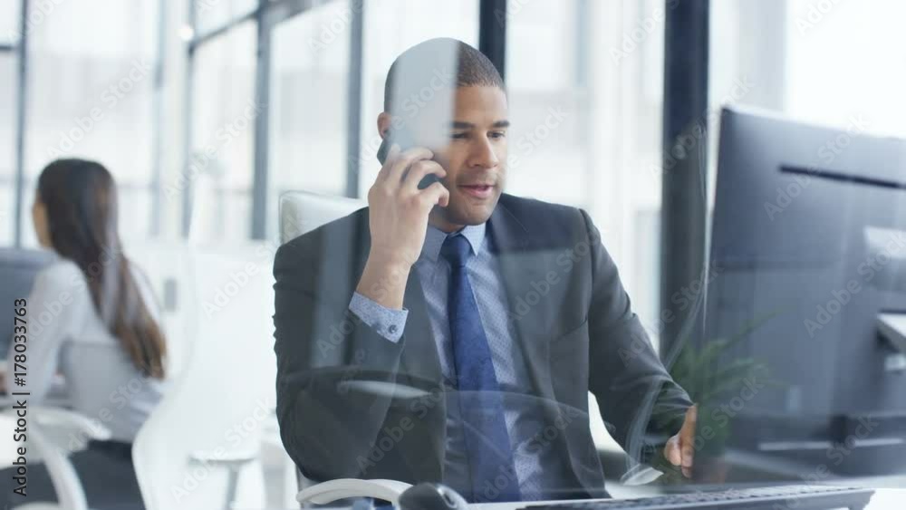 Businessman working on computer in the office gets good news from phone call. Businessman working on computer in the office gets good news from phone call.