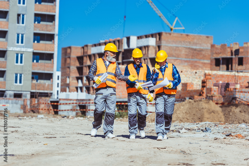 Three workers in hardhats at construction site Three workers in hardhats at construction site