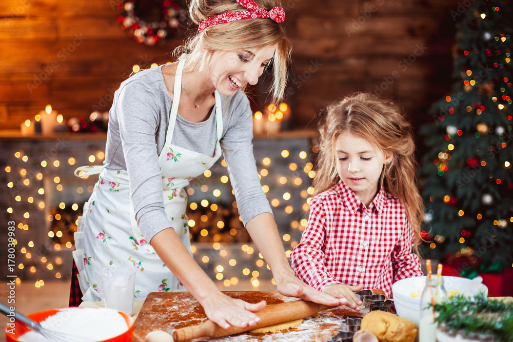Merry Christmas and Happy Holidays. Family preparation holiday food. Mother and daughter cooking cookies in New Year interior with Christmas tree.