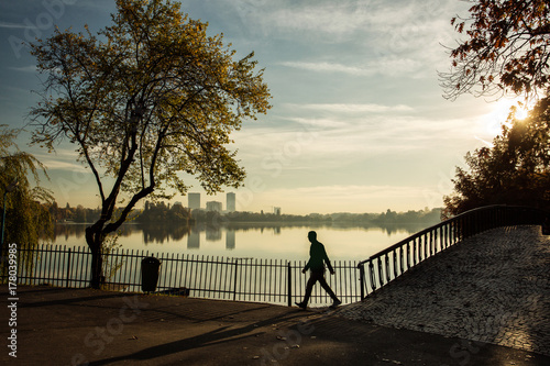 Man walking in a park at sunrise with beautiful autumn colors and lake in background