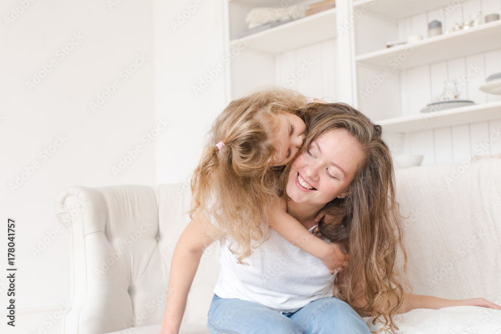 Little girl hugging her mother in the interior on the couch. Happy loving family. Mother and her daughter child girl playing and hugging. Little girl hugging her mother in the interior on the couch. Happy loving family. Mother and her daughter child girl playing and hugging.