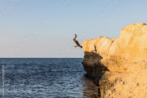 Young man jumping from rock to sea.
