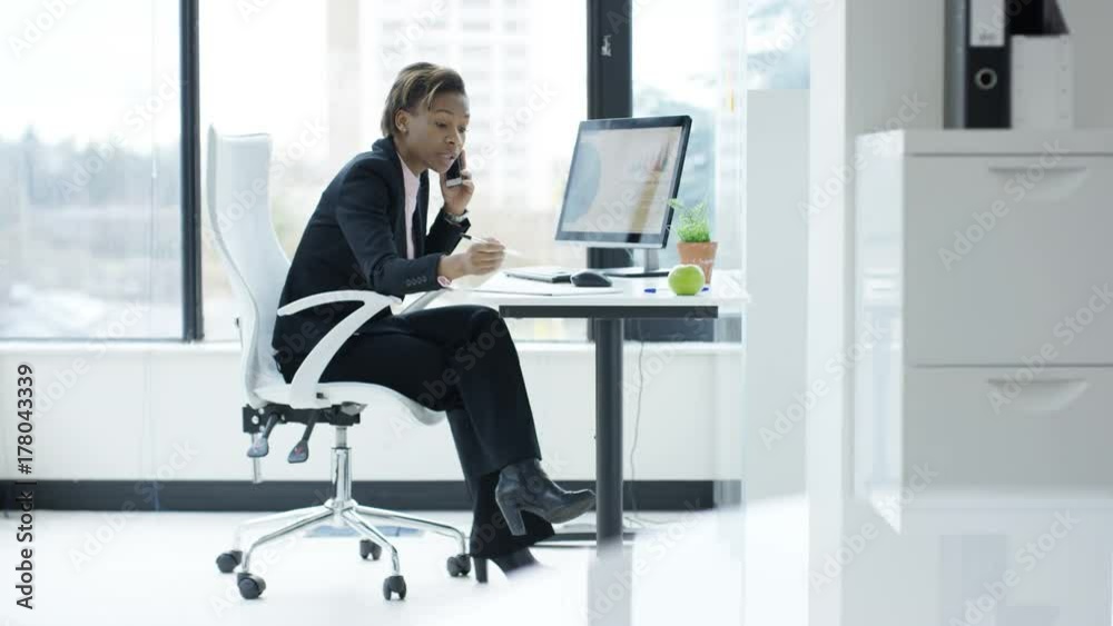 Businesswoman working at her desk, looking at computer and talking on phone. Businesswoman working at her desk, looking at computer and talking on phone.