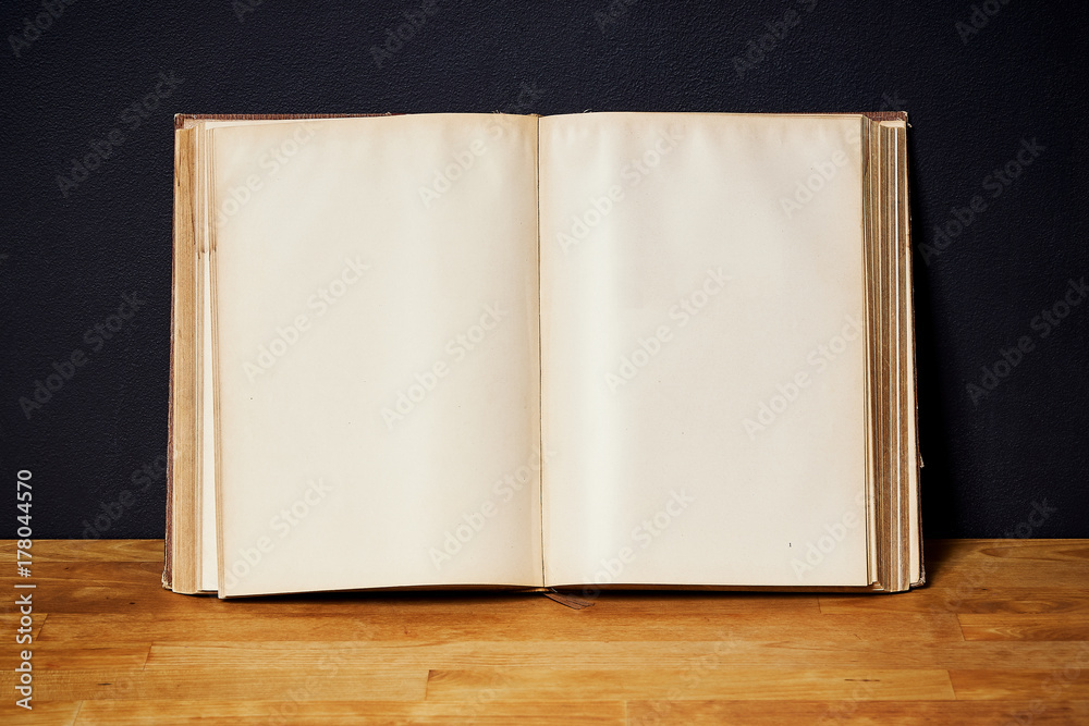 Opened empty old book on a bright wooden shelf on a black wall Opened empty old book on a bright wooden shelf on a black wall