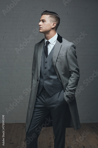 A handsome man in a three piece suit standing with hand in pocket photo