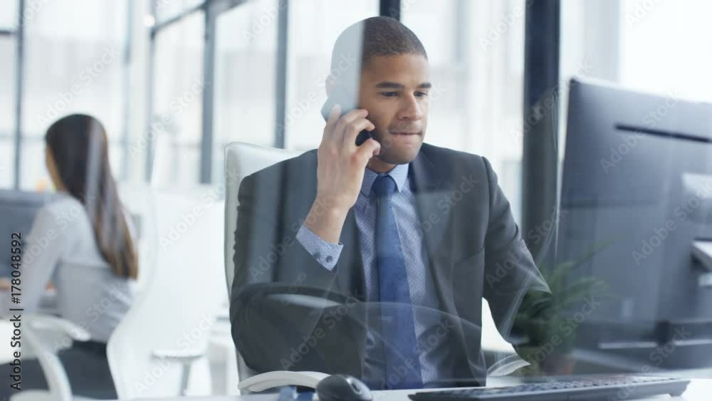 Businessman working on computer in the office gets good news from phone call Businessman working on computer in the office gets good news from phone call