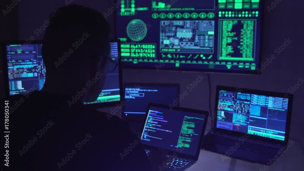 Male hacker working on a computer in a dark office room.